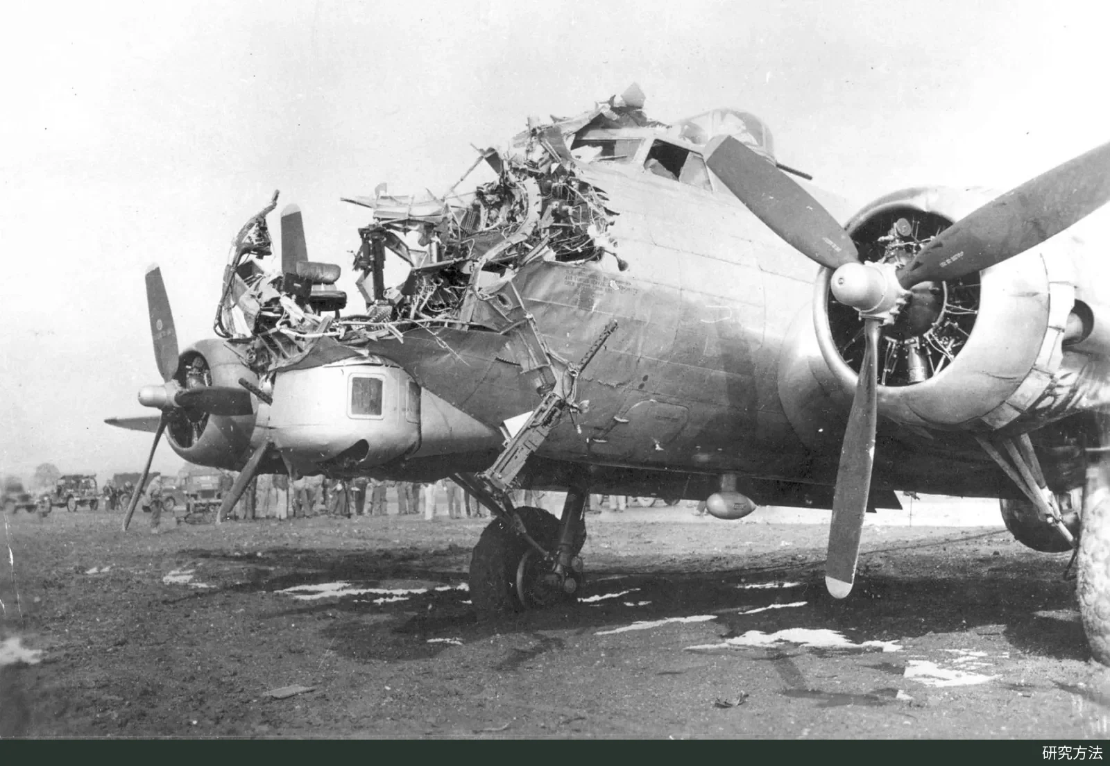 The nose of a B-17 bomber blown open by an anti-aircraft shell, its metal skin curled and torn, with the aircraft parked on the ground
