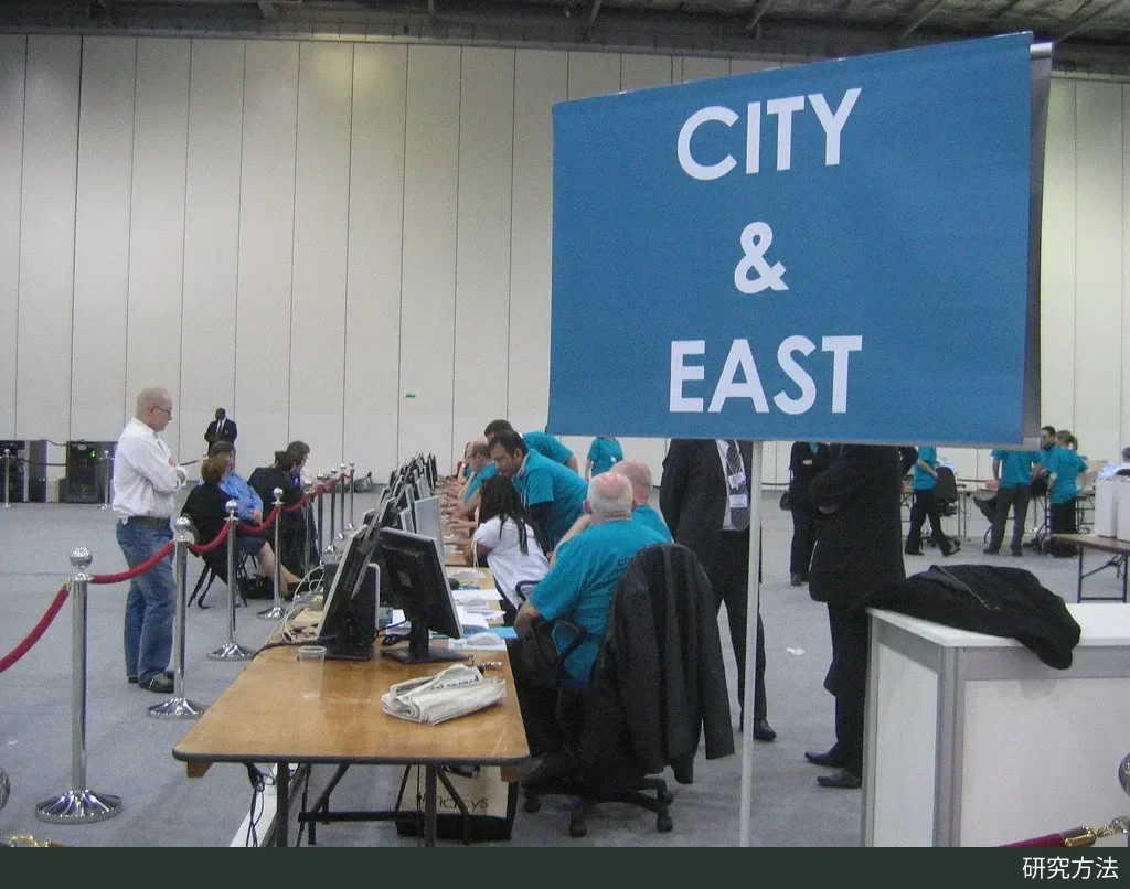 伦敦 ExCeL 计票中心内,蓝色“CITY & EAST”指示牌旁,穿蓝绿色上衣的工作人员坐在一排电脑屏幕前。