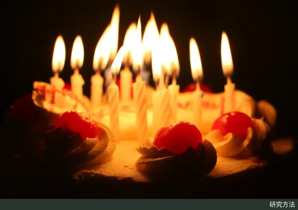 暗色背景中的奶油生日蛋糕，插着十多支点燃的白色螺纹蜡烛，蛋糕边缘点缀着红色樱桃